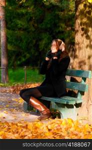 young woman is sitting on the bench in autumn park and listening music