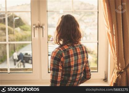 Young woman is standing and looking out the window
