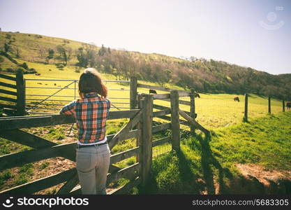 Young woman is standing by a fence on a ranch with cattle in the distance