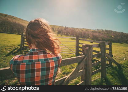 Young woman is standing by a fence on a ranch with cattle in the distance