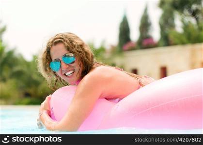 young woman is swimming in a pool on pink air bed