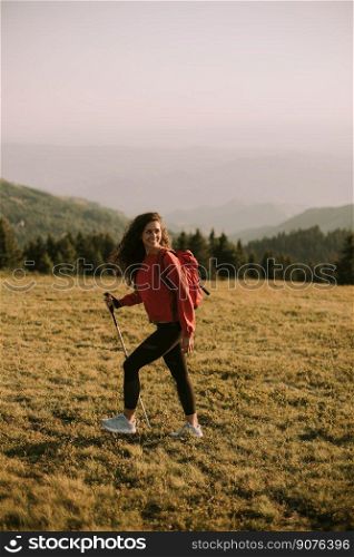 Young woman is taking a scenic hike on a hill, carrying all her necessary gear in a backpack. She appears to be a seasoned hiker, enjoying the challenge and beauty of the outdoor experience