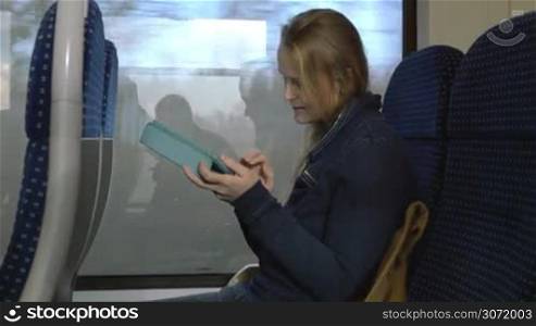 Young woman is traveling by train. She&acute;s sitting in coach with tablet PC in hands.