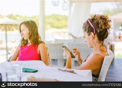 Young woman is using mobile smart phone to send or read message or to make a call on social network during a break at the cafe or restaurant in sunny day outdoors