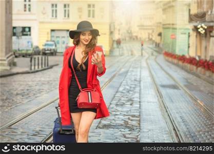 Young woman is using smartphone walking with suitcase on the city street of old European city.. Young woman is using smartphone on street.