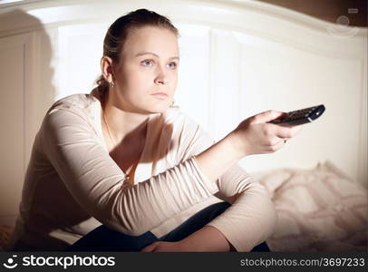 Young woman is watching tv with remote control.