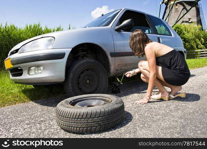 Young woman jacking up her car to change a flat tire with a spare one