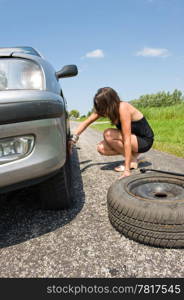 Young woman jacking up her car to change a flat tire with a spare one