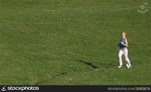 Young woman jogging in the park across a lush green lawn in a health and fitness concept