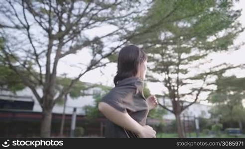 Young woman jogging on alone under trees inside public park, , stay healthy during lockdown pandemic, human metabolic system, sunset golden hour view from behind, self dedication goal to success