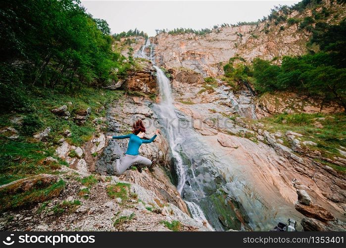 Young woman jumping in a mountain near a waterfall