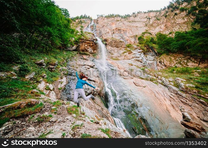 Young woman jumping in a mountain near a waterfall