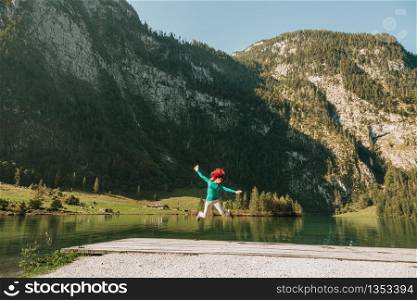 Young woman jumping on a pier near a lake under the mountains