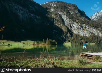 Young woman jumping on a pier near a lake under the mountains