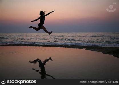 Young woman jumps on beach on sunset