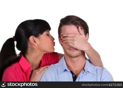 Young woman kissing her boyfriend on the cheek hiding his eyes