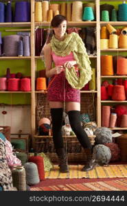 Young Woman Knitting Scarf Standing In Front Of Yarn Display