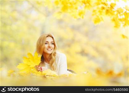 Young woman laying down on the ground covered dry autumnal foliage in beautiful park