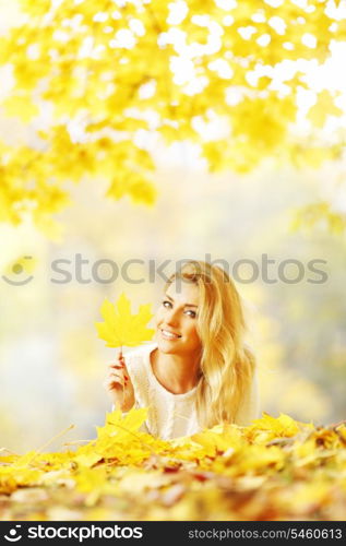 Young woman laying down on the ground covered dry autumnal foliage in beautiful park