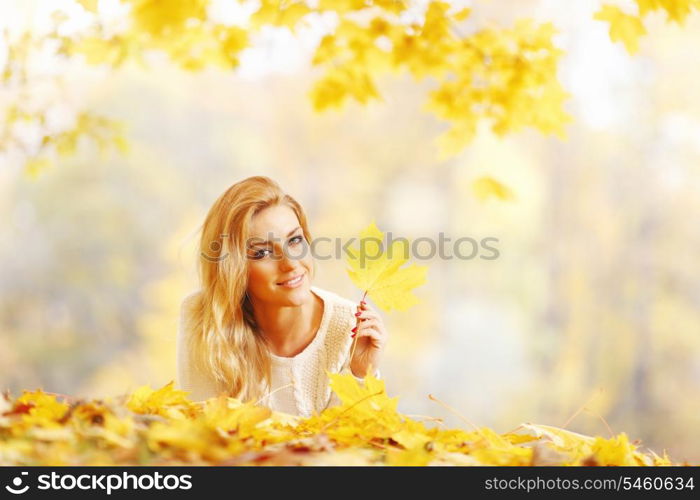 Young woman laying down on the ground covered dry autumnal foliage in beautiful park