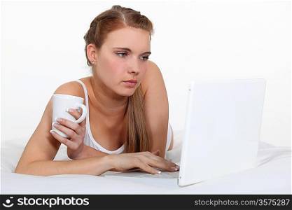 Young woman laying on bed with laptop and coffee