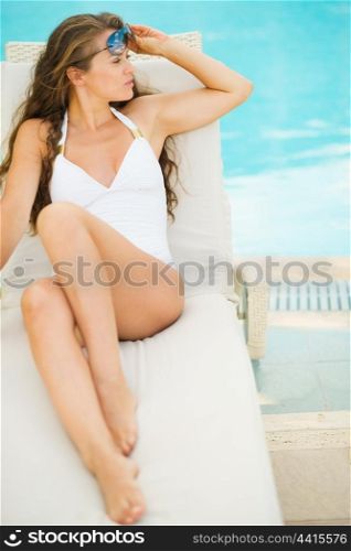 Young woman laying on chaise-longue at poolside and looking on copy space