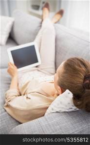 Young woman laying on couch with tablet pc . rear view