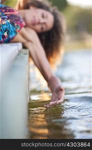 Young woman laying on jetty, hand touching water