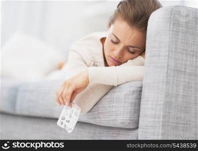 Young woman laying on sofa and holding empty medicine blister package