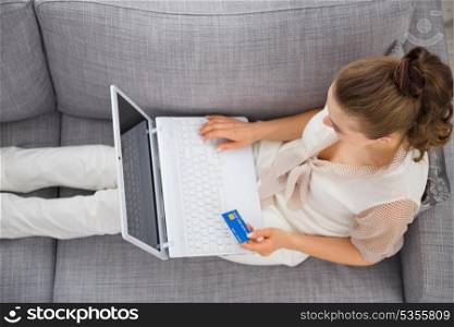 Young woman laying on sofa with laptop and credit card