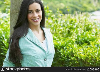 Young woman leaning against a tree trunk in a park and smiling