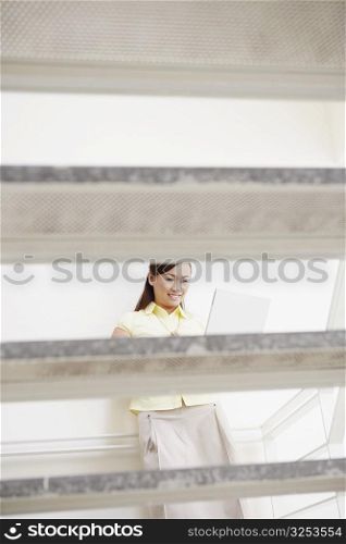 Young woman leaning against a wall and using a laptop