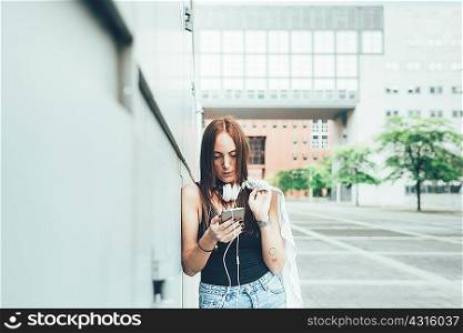 Young woman leaning against wall reading smartphone texts
