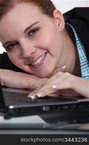 young woman leaning her head on a laptop and smiling