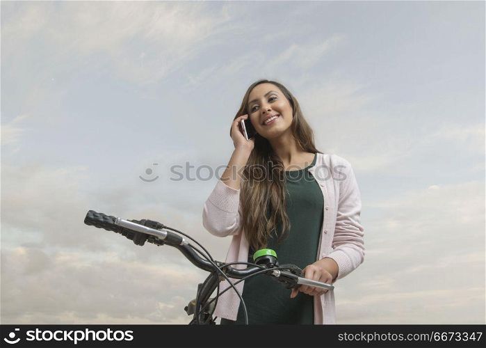 Young woman leaning on bike and talking on phone