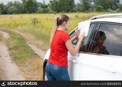 Young woman leaning on car and looking at map