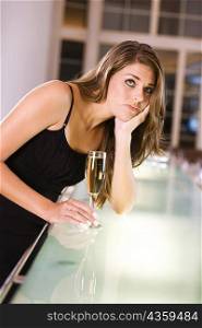 Young woman leaning over a bar counter holding a champagne flute