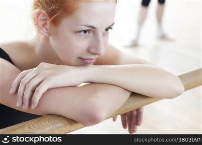 Young woman leans on ballet barre at mirror in rehearsal room