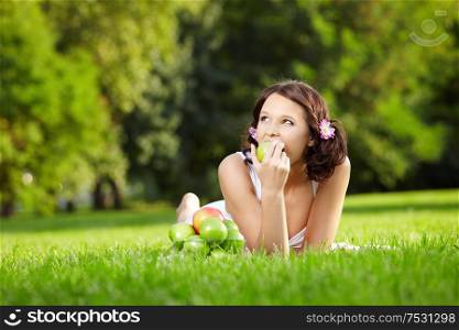 Young woman lies in a summer garden and eats an apple