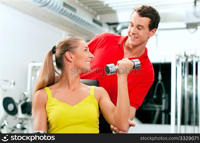 Young woman lifting a dumbbell in the gym assisted by her personal trainer (focus on woman)