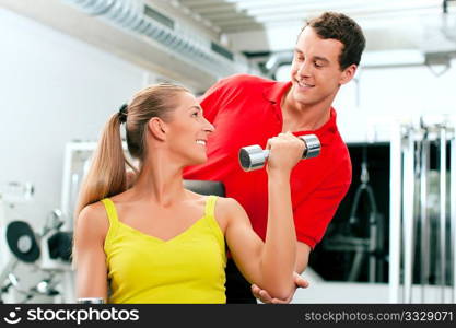 Young woman lifting a dumbbell in the gym assisted by her personal trainer (focus on woman)