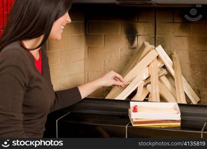 Young woman lighting up wood logs in fireplace home living