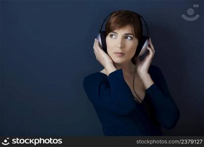 Young woman listen music with headphones over a blue wall