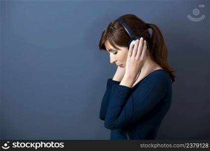 Young woman listen music with headphones over a blue wall