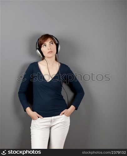 Young woman listen music with headphones over a grey wall