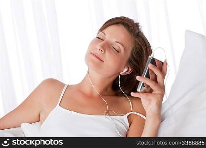 Young woman listening to music holding mp3 player on white sofa