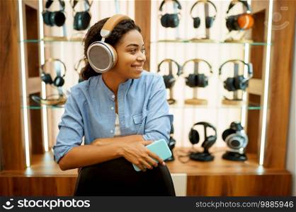 Young woman listening to music in headphones store. Female person in audio shop, showcase with earphones on background, buyer in multimedia salon. Young woman listening to music, headphones store