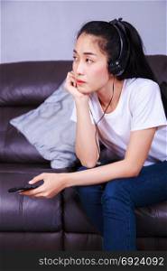 young woman listening to music in headphones with moblie on sofa at home