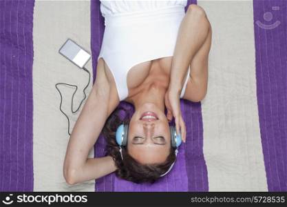 Young woman listening to music through MP3 player using headphones while lying on picnic blanket