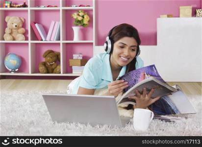 Young woman listening to music while reading magazine at home
